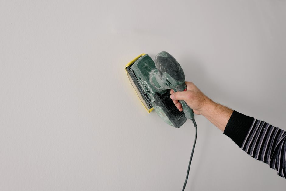 Crop anonymous workman working with sander while smoothing walls during repair process in apartment