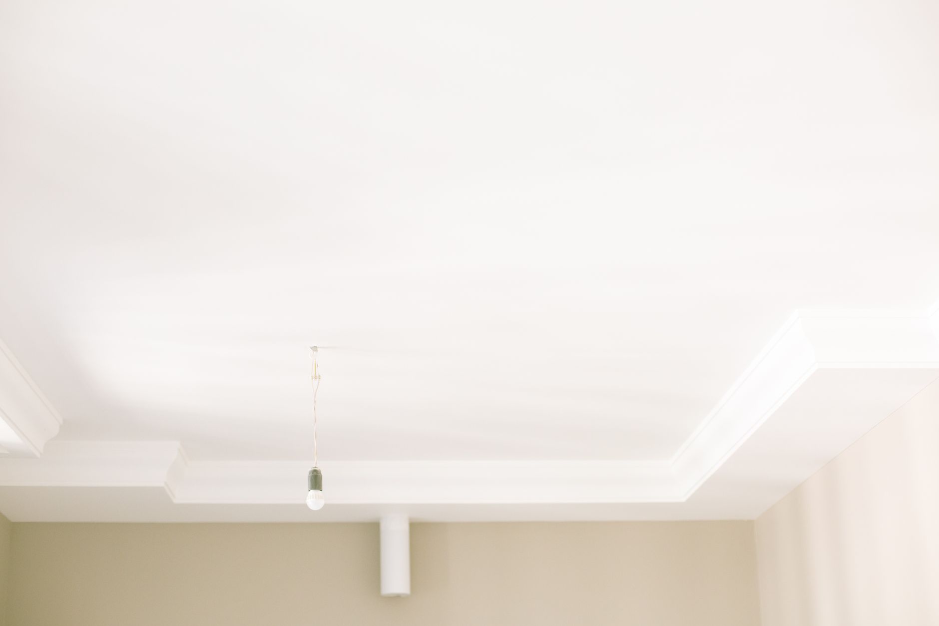 Bright white ceiling with a single hanging light bulb highlighting minimal interior design in Riverside, CA