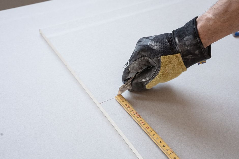 Gloved hand holding a ruler against a wall