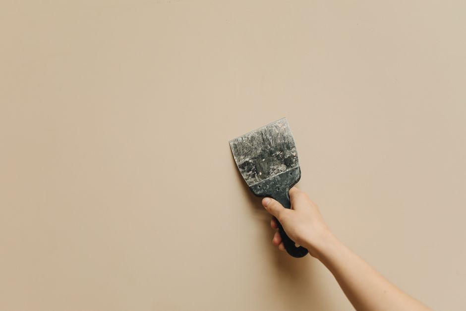 A hand holding a spatula against a blank beige wall for home renovation.
